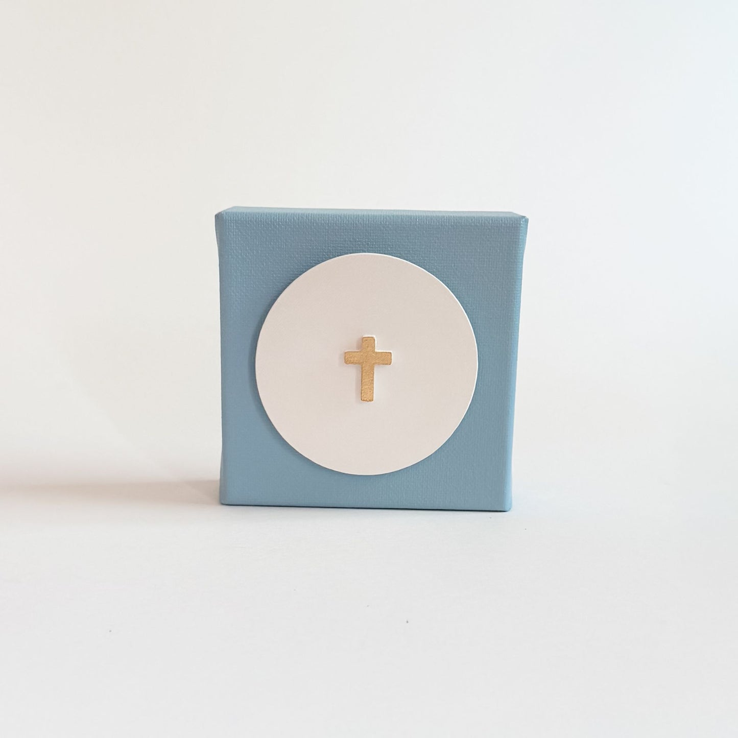 Small blue box with a white circle and gold cross on a light blue background