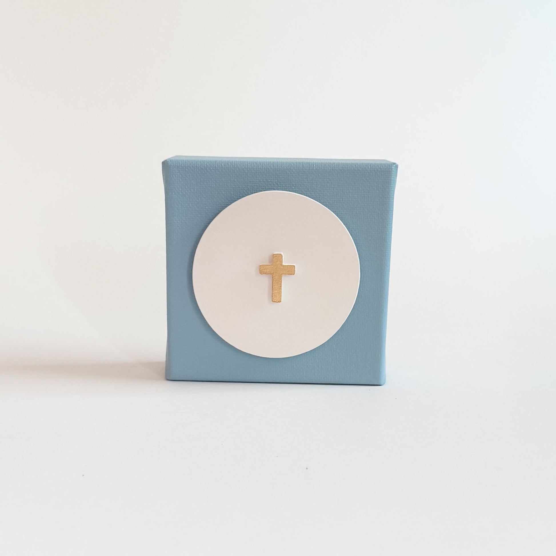 Small blue box with a white circle and gold cross on a light blue background