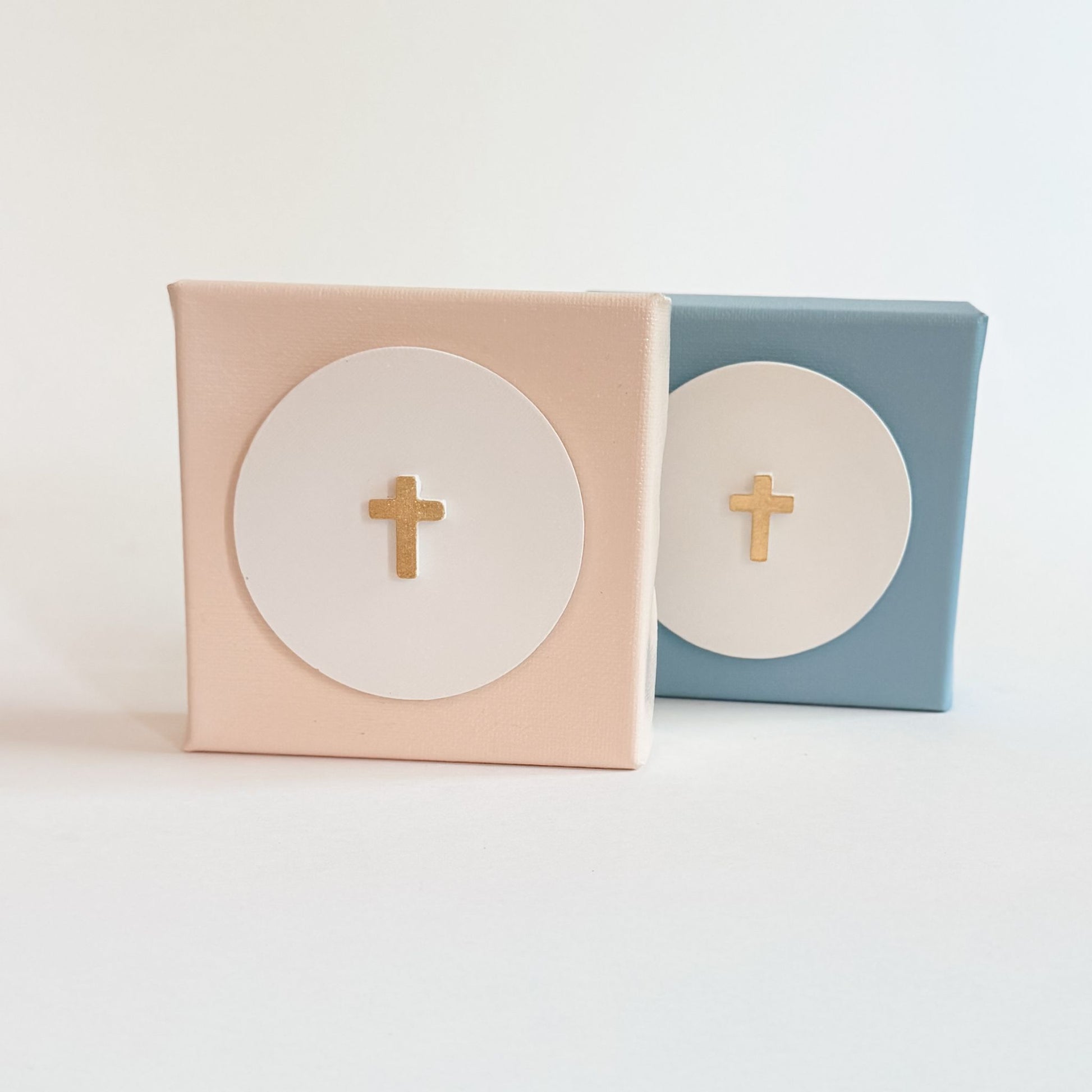 Two small boxes, one pink and one blue, with gold crosses on a light background